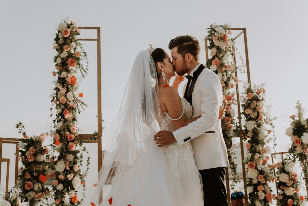 Novios recién casados, se besan en su ceremonia, con decoración dorada y flores pasteles, estilo elegante. Boda de destino en La Habana