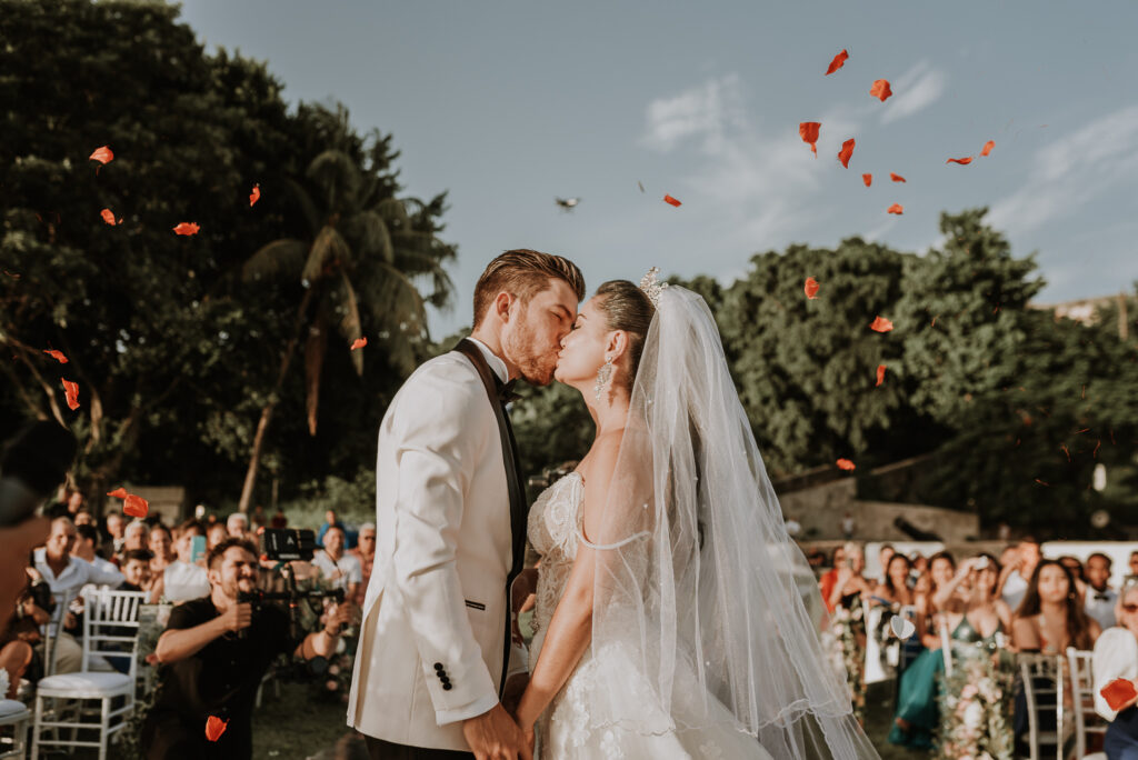 Novios se besan al finalizar su ceremonia. de bodas en La Habana. Novios al centro de la foto, al fondo pétalos de flores lanzados por los invitados.