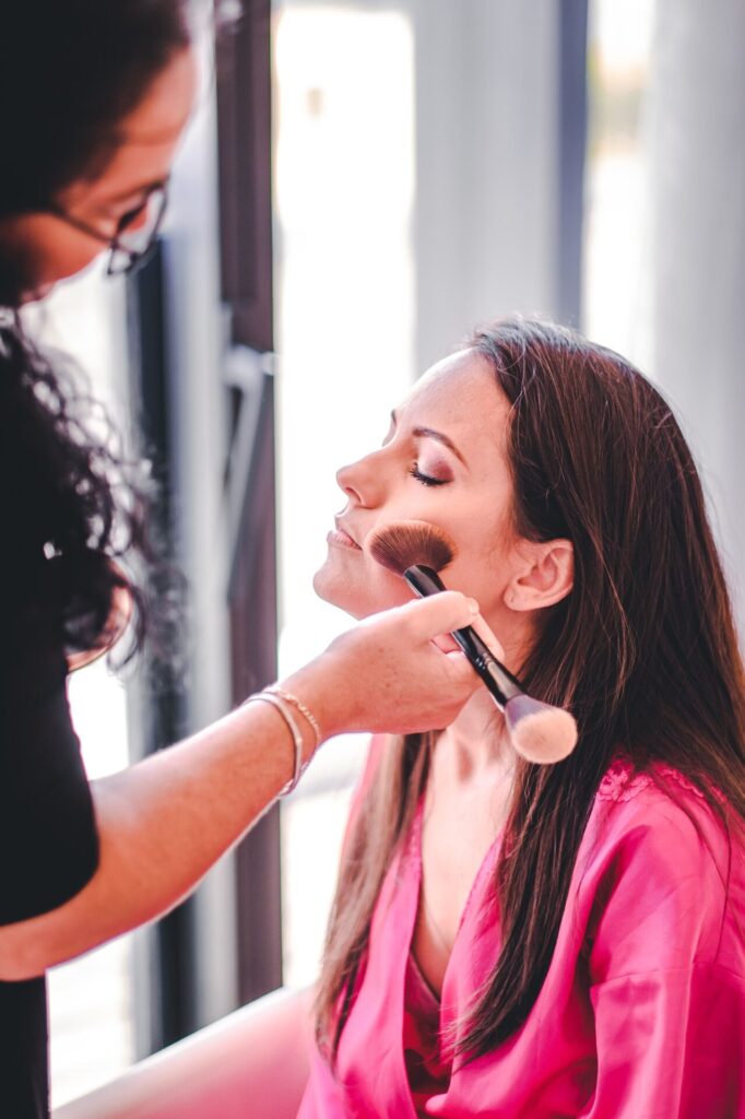 Novia en bata fucsia siendo maquillada de cerca en el Hotel Grand Packard