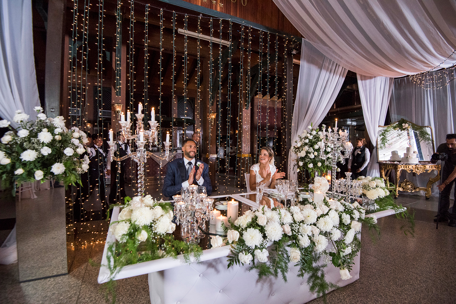 Novios aplaudiendo en la mesa presidencial decorada con flores blancas en el Hotel Nacional de Cuba.