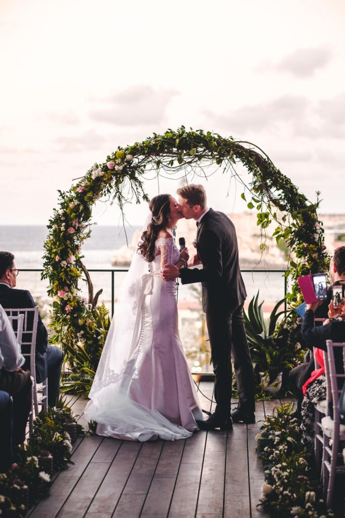 Novios besándose bajo arco floral en ceremonia en el Hotel Grand Packard
