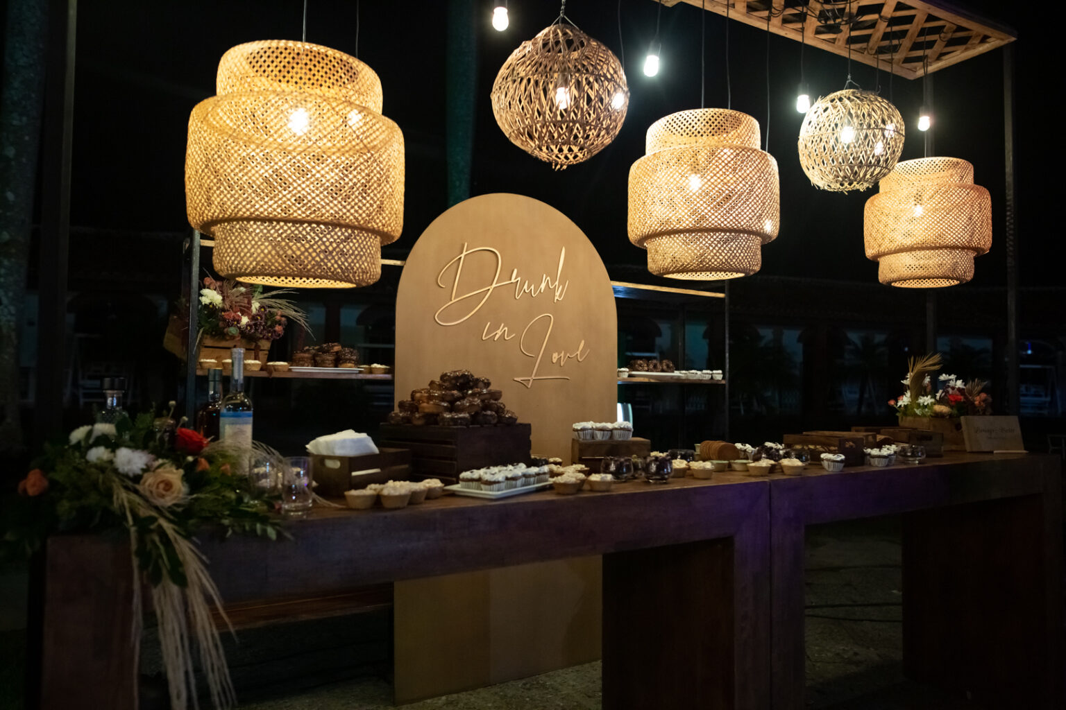 Mesa de postres iluminada con lámparas de mimbre en la boda en Viñales