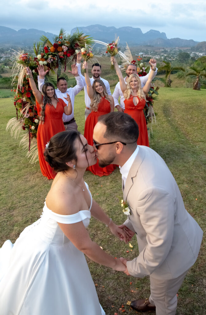 Novios besándose frente al cortejo en su boda en Viñales, con arco floral de fondo