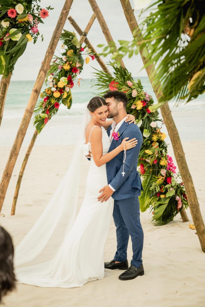 Alba y Renato abrazados durante la ceremonia, con el túnel de bambú y flores tropicales al fondo.