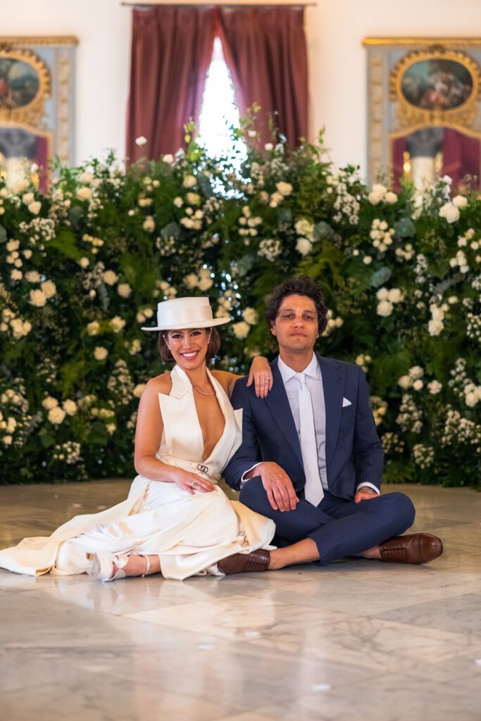 Posando frente a un fondo floral decorado con greenery en el Palacio de los Matrimonios, durante su boda de destino en La Habana, Cuba.