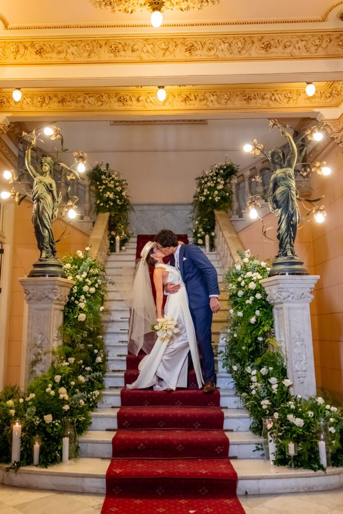 Compartiendo un beso en la escalera decorada estilo greenery, durante su boda de destino en La Habana, Cuba.