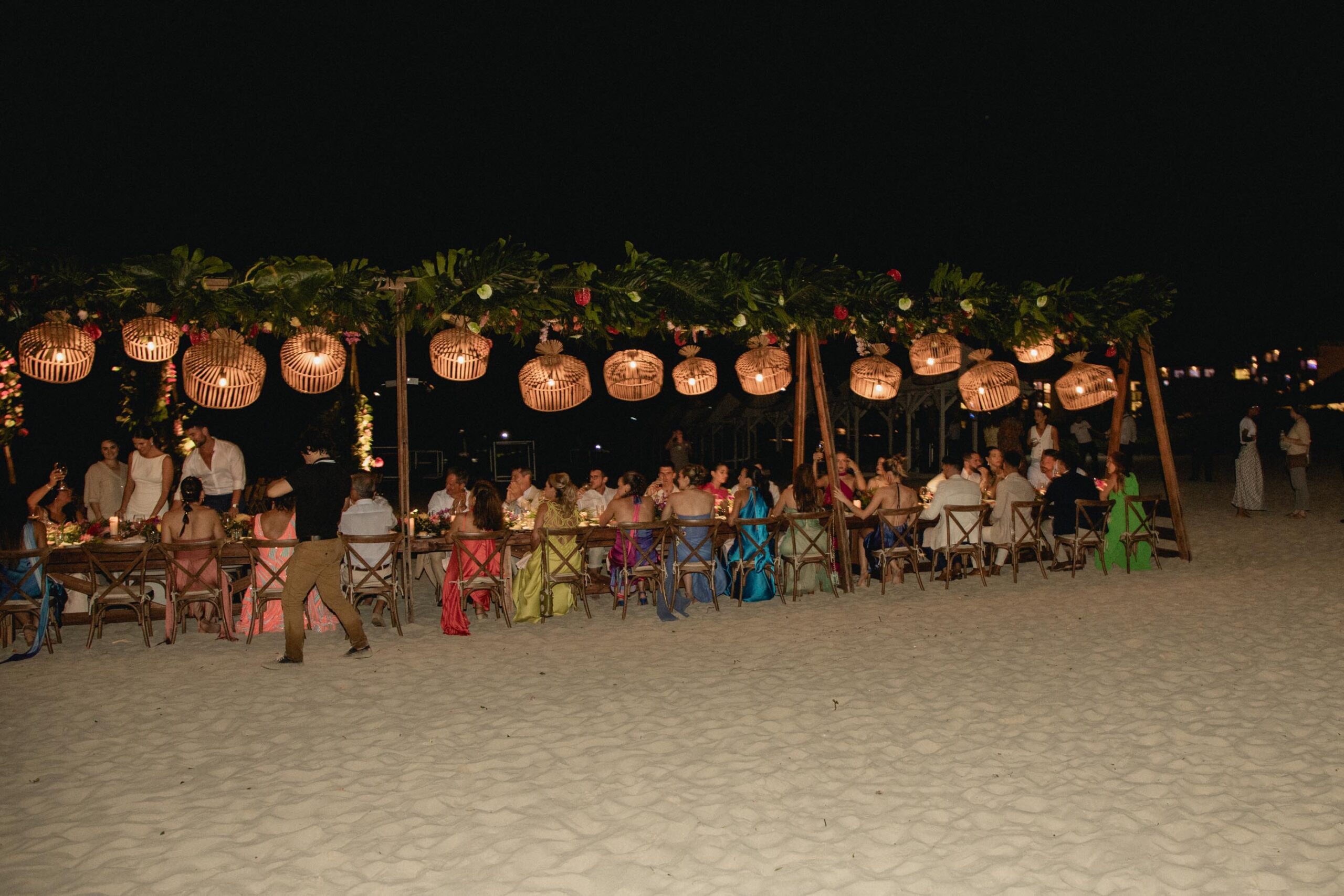 Vista lejana de los invitados cenando en la mesa decorada e iluminada durante la boda en Melia Internacional de Varadero.