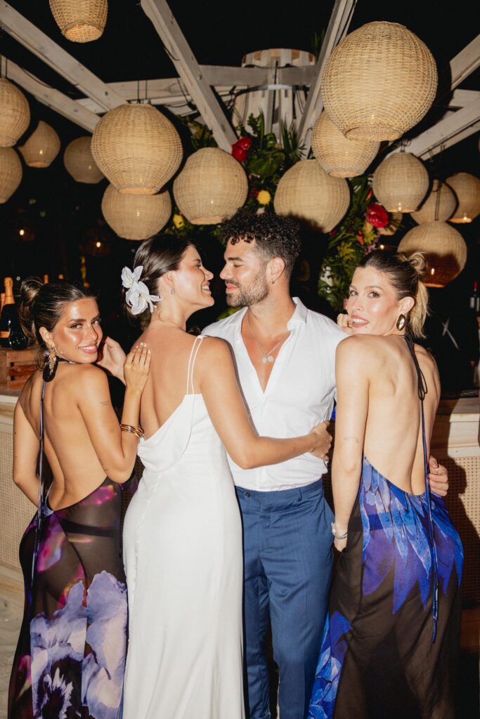 Alba y Renato posando con sus amigas frente al bar redondo iluminado durante la boda