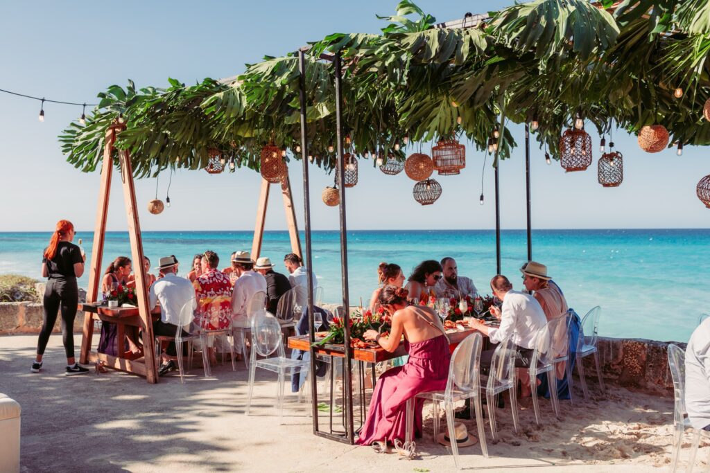 Invitados disfrutando del almuerzo frente al mar en la terraza de la Casa de Al Capone, con decoración de Aire de Fiesta para una boda tropical en Varadero, diseñada con atención al detalle.