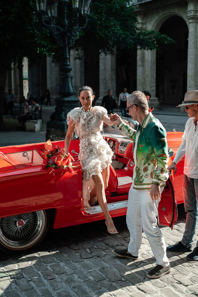 Novia bajando de un auto rojo para su boda destino cubana
