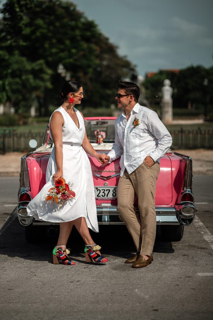 Amanda y Leo frente al carro clásico rosado en su boda en La Guarida, La Habana.