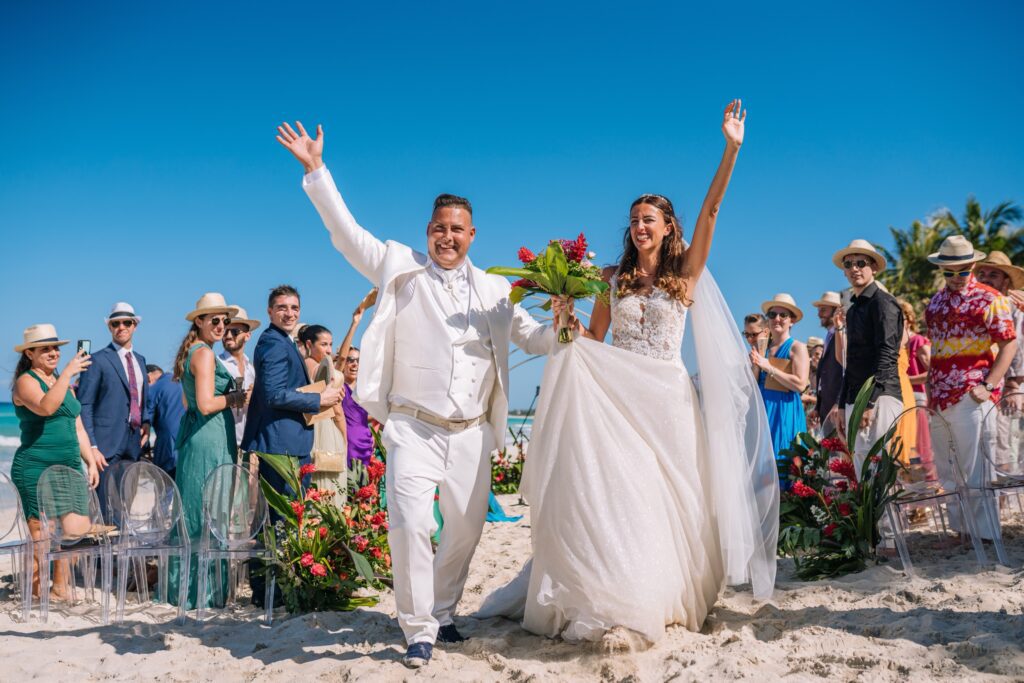 Los novios, con los brazos levantados y sonriendo, saliendo de la ceremonia, llenos de felicidad, en su boda de destino en Varadero