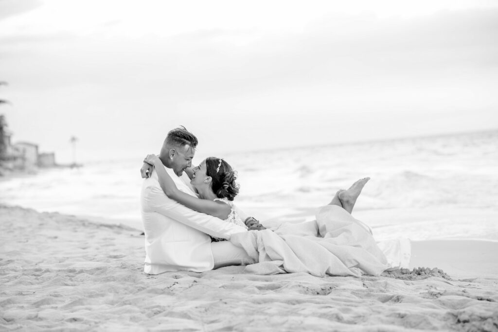 Giada, tumbada en la arena, abraza a Gorke mientras él está sentado, compartiendo un momento íntimo durante su boda de destino en Varadero.