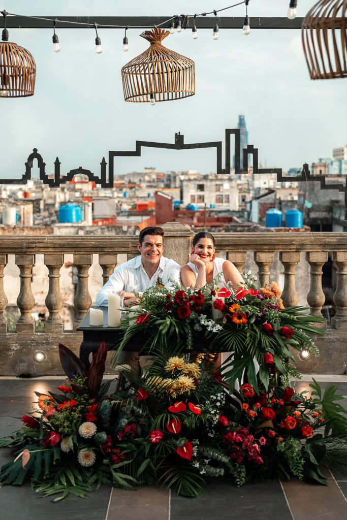 Los novios en la mesa presidencial en la Guarida, rodeada de flores tropicales, con el skyline de La Habana como fondo, destacando los tejados.