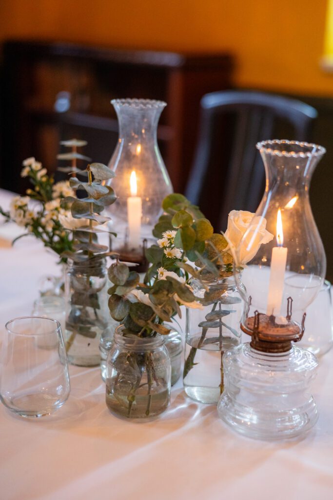 Detalle del centro de mesa con quinqués antiguos, flores blancas y velas, decoración de boda en La Habana.