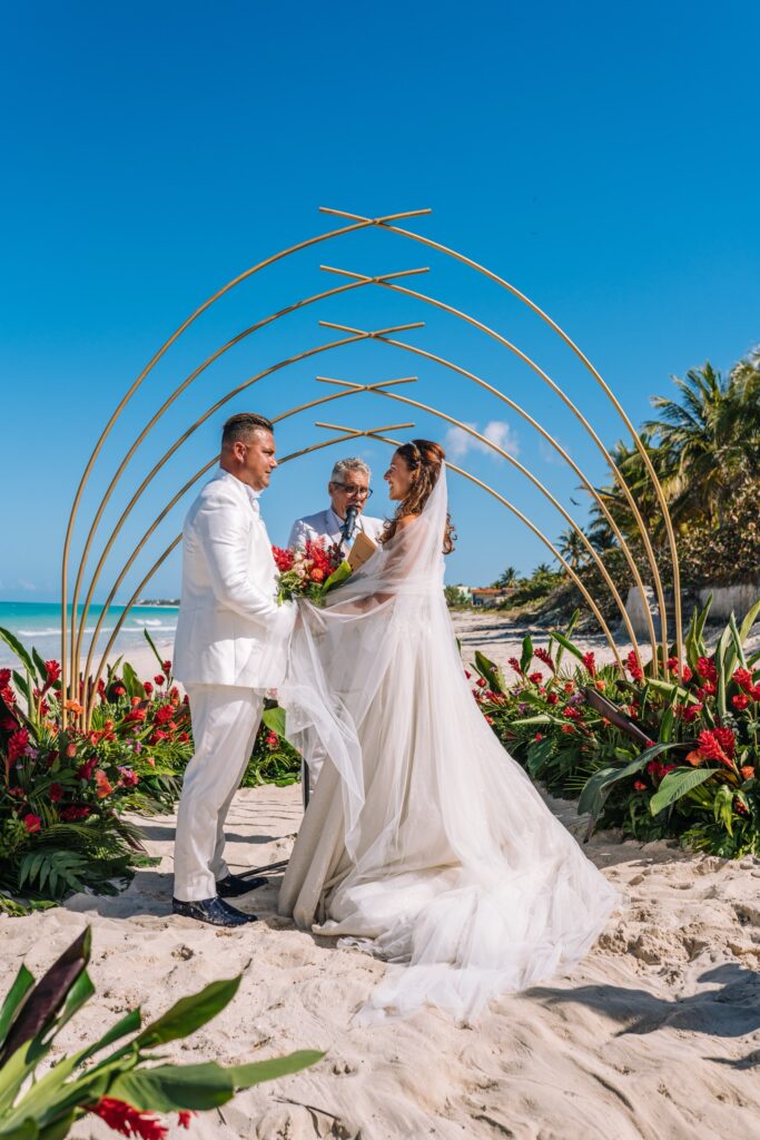 Giada y Gorke intercambiando votos frente al mar, con un altar geométrico y tropical en una boda en Cuba.