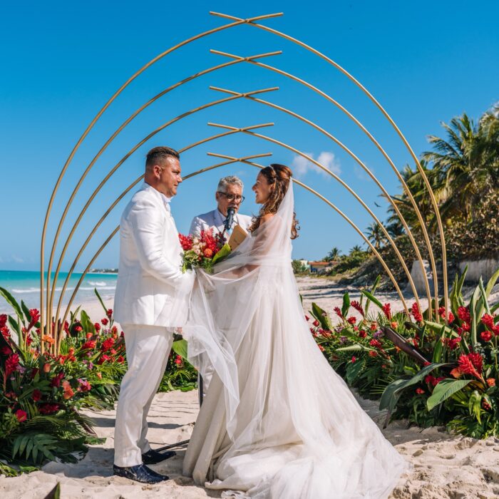 Giada y Gorke intercambiando votos frente al mar, con un altar geométrico y tropical en una boda en Cuba.