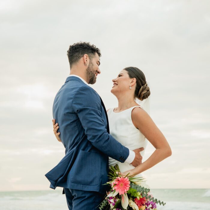 Alba y Renato mirándose tras la ceremonia, con un bouquet tropical en la playa.