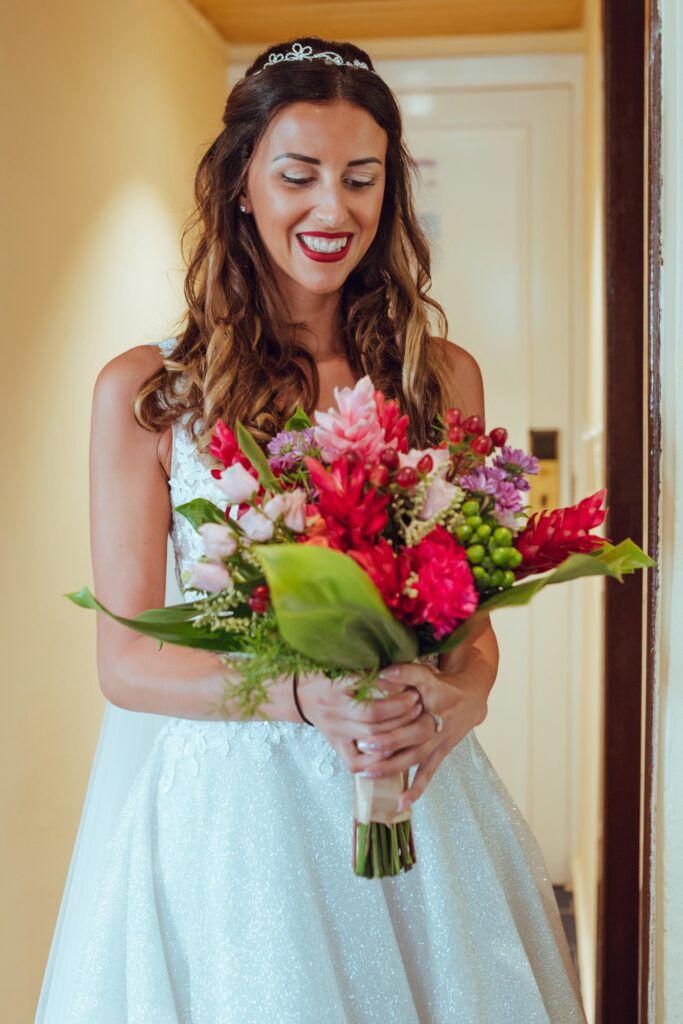 Un momento especial en el que Giada observa su ramo de novia, que combina flores en tonos rojizos, rosados y fucsias, reflejando la decoración tropical de la boda.