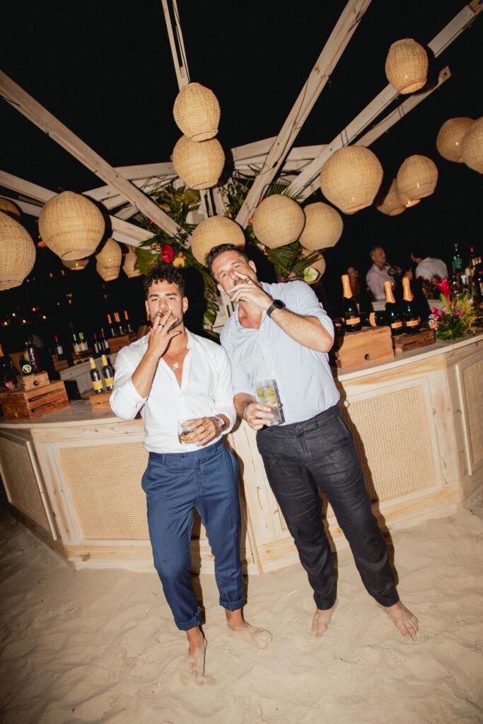 Renato y un amigo disfrutando de un puro frente al bar redondo iluminado durante la boda