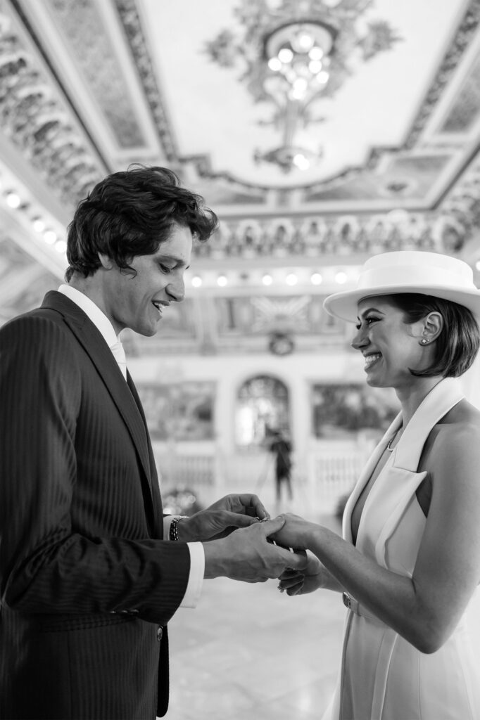 Los novios intercambiando anillos durante la ceremonia de su boda de destino en el Palacio de los Matrimonios de Prado.