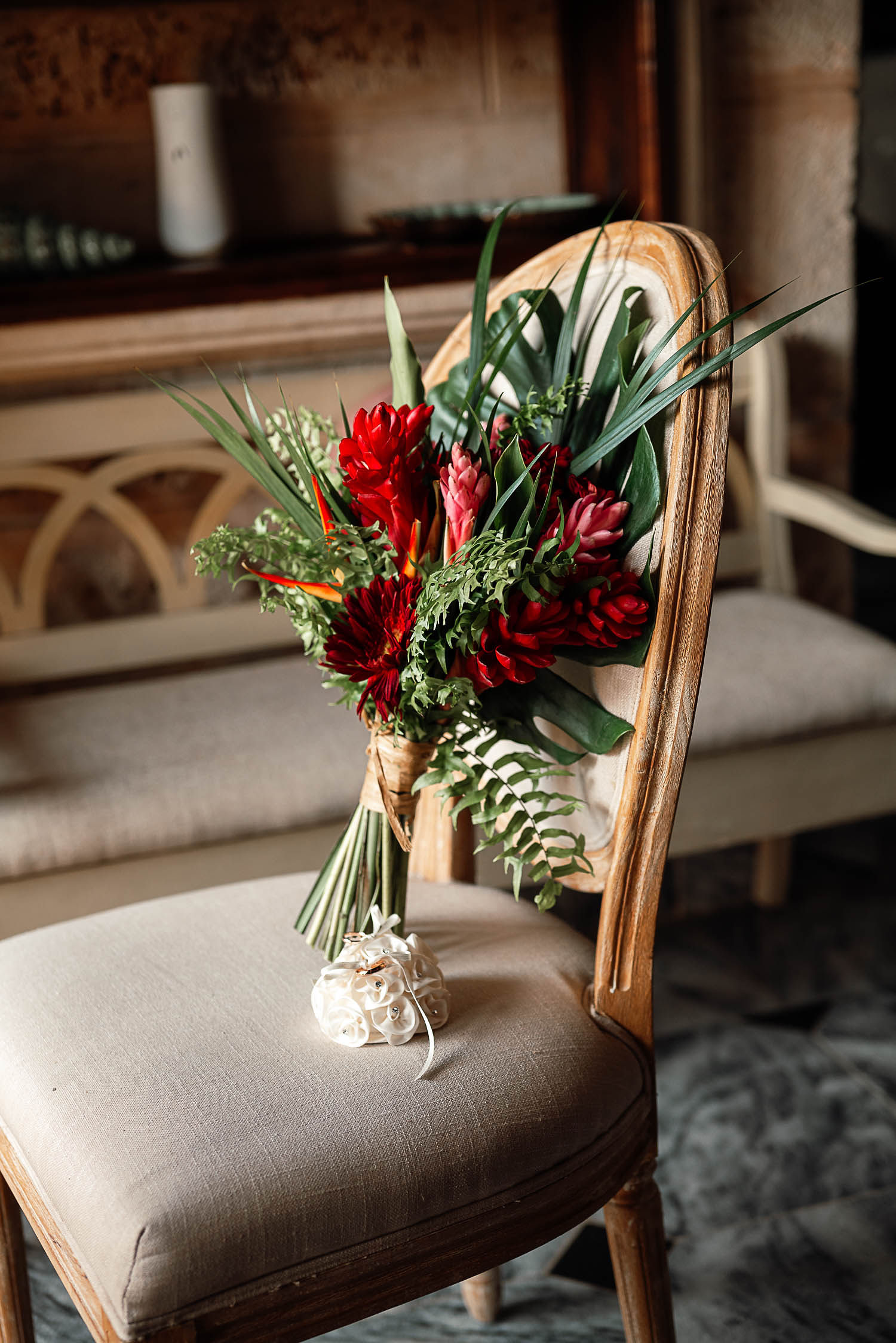 Ramo de novia con flores tropicales rojas y follaje verde sobre una silla clásica, ideal para una boda en un destino exótico.