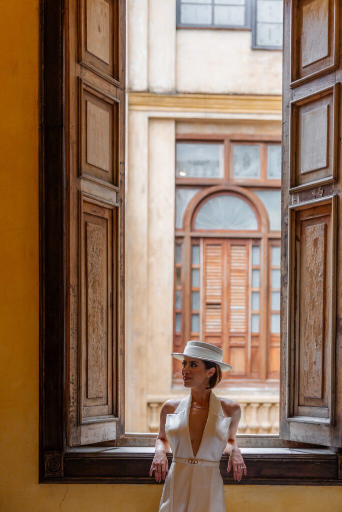 Victoria posando en el salón de cena junto a una ventana histórica, con vistas coloniales, luciendo un vestido de Lorenzo Caprile en La Guarida, La Habana, Cuba.