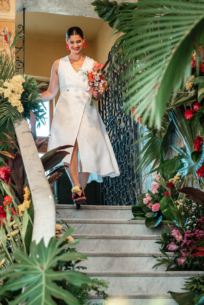 Amanda baja por la escalera decorada con flores tropicales en su boda en La Guarida, La Habana.