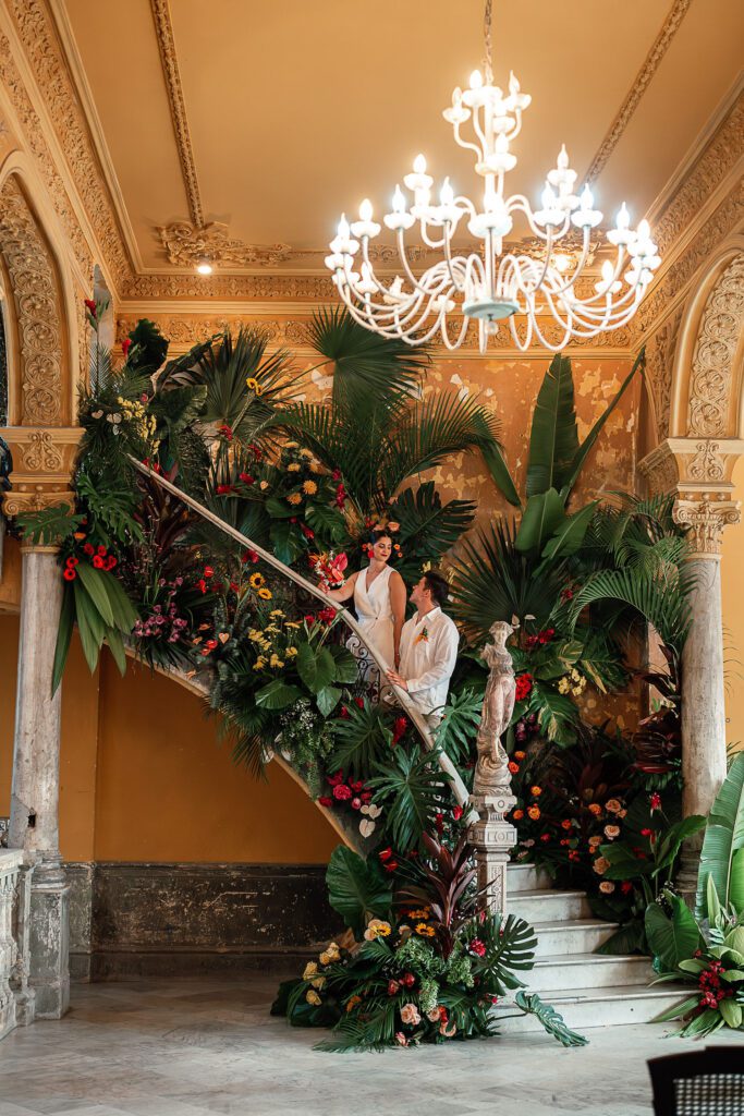 The newlyweds posing on the staircase of La Guarida, surrounded by tropical flowers, after their wedding.