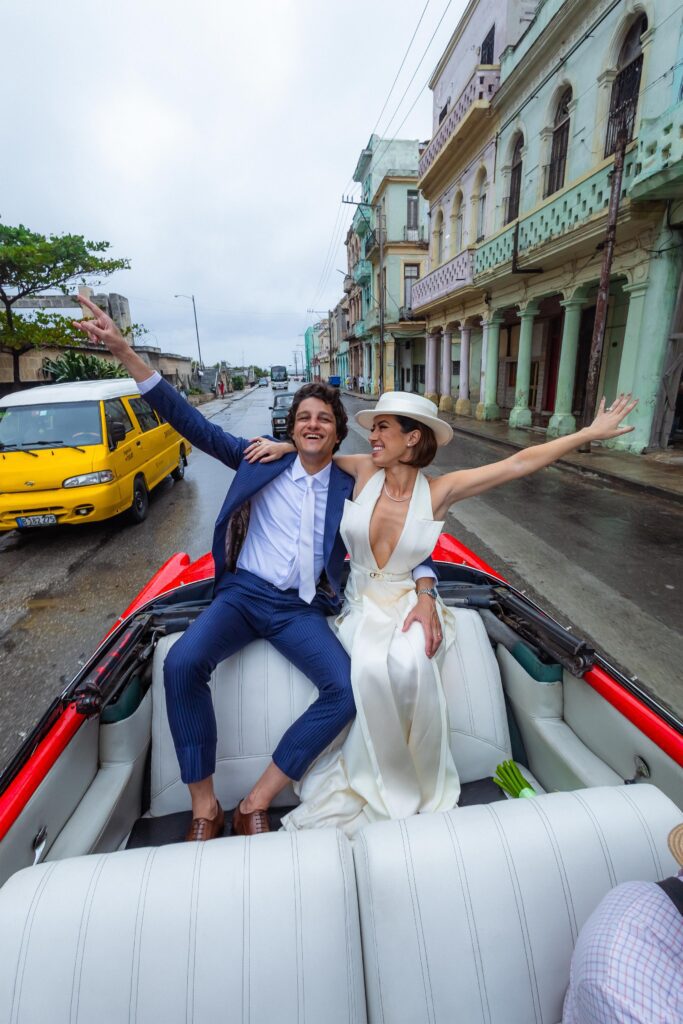 Novios saludando en auto descapotable en boda de destino en La Habana.