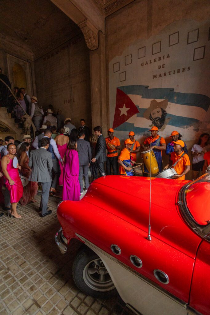 Invitados subiendo la escalera hacia La Guarida, con músicos y un carro clásico en la entrada, destacando la energía de la boda de destino en La Habana.