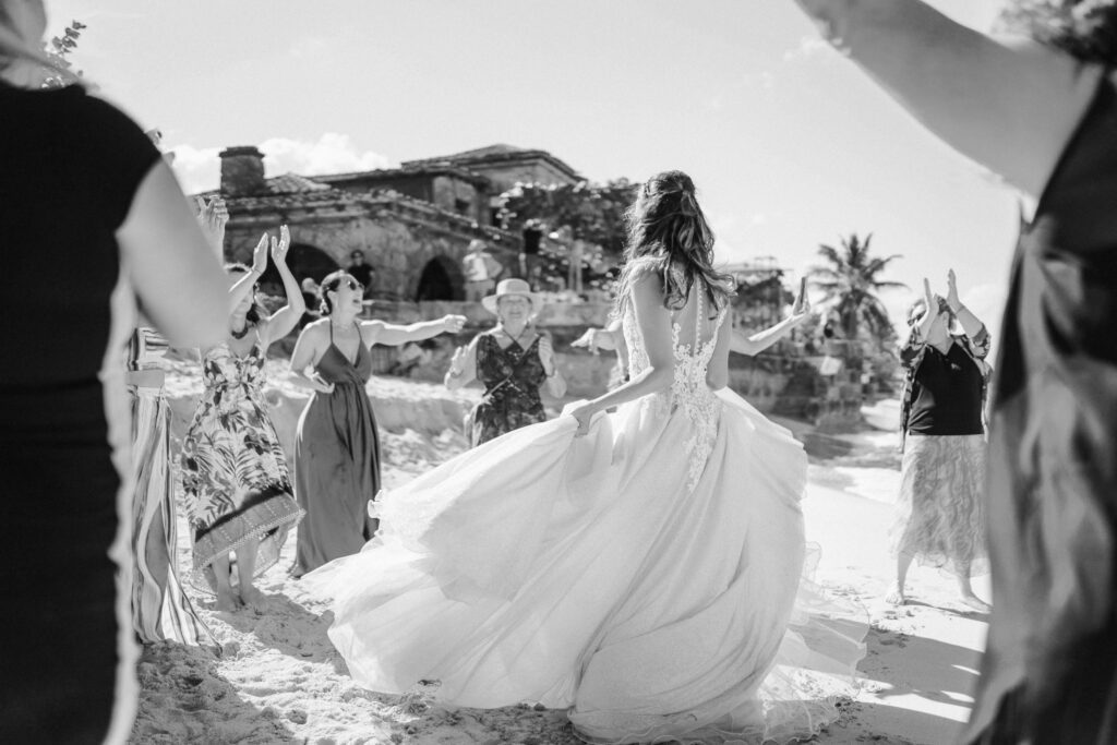 La novia bailando en la playa mientras los invitados la rodean en una rueda de baile, disfrutando de un momento de alegría en su boda de destino en Varadero.