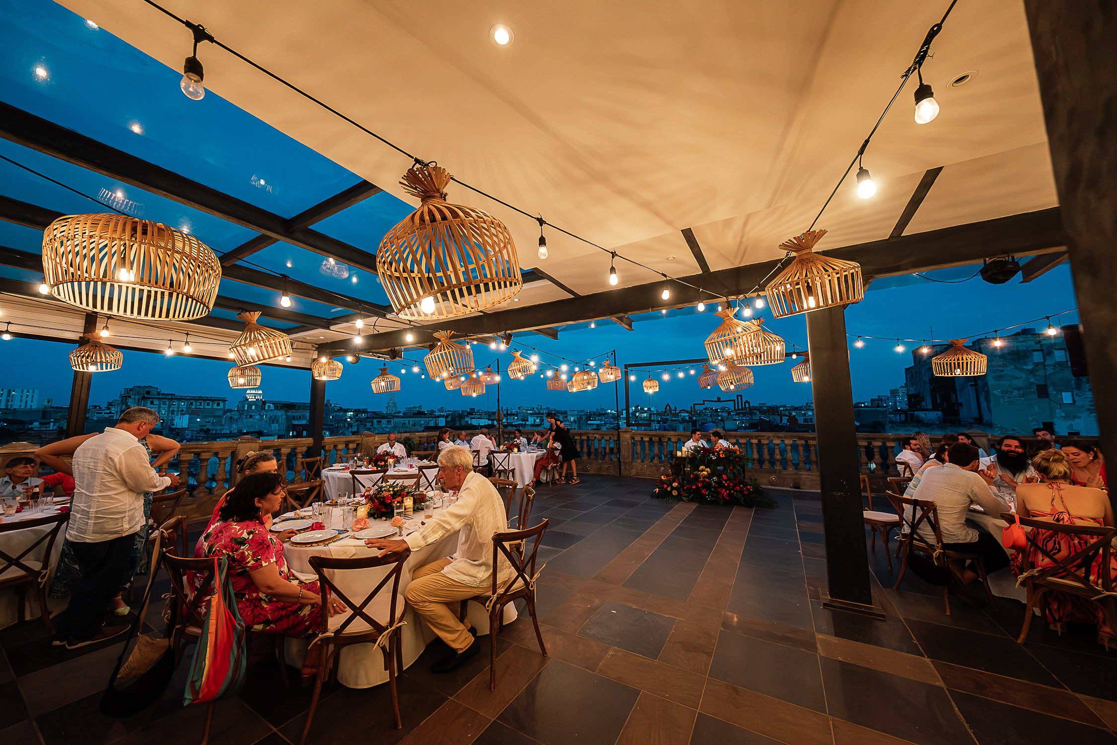 Ambiente de la terraza decorada para la cena de la boda con iluminación cálida y flores tropicales.