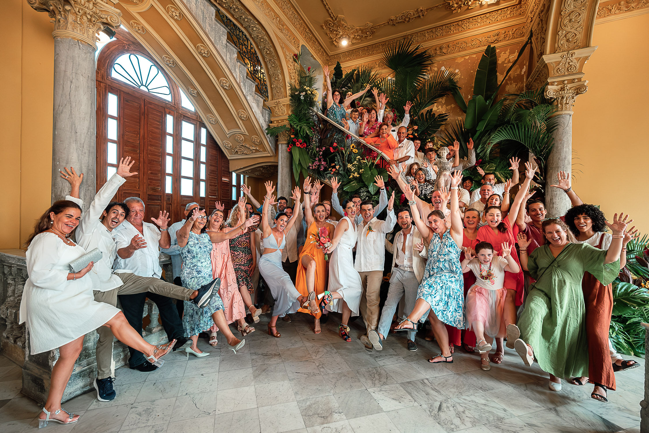 Grupo de invitados posando en la escalera de La Guarida, rodeados de flores tropicales, después de la boda.