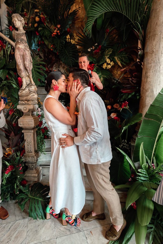 El beso de los novios sellando su amor durante la ceremonia de boda en La Guarida, con la decoración tropical como fondo.