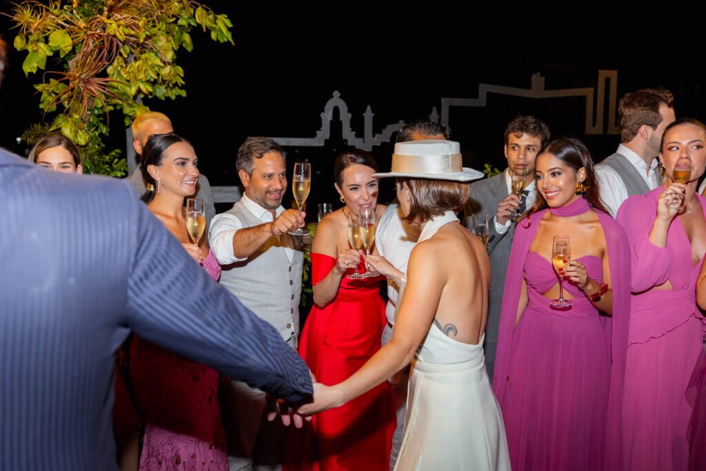 IInvitados celebrando con un brindis junto a los novios en la boda de destino en La Habana, mientras que, detrás, se aprecia el impresionante skyline de la ciudad, lo que resalta aún más la magia del momento.