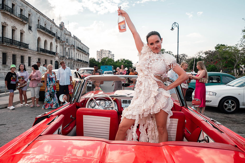 Novia brindando en auto clásico durante su boda de destino cubana