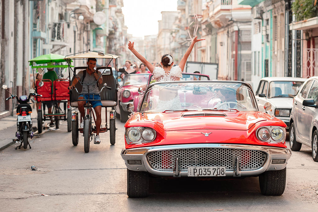 Novios recorren La Habana en auto clásico rojo tras su boda de destino cubana.
