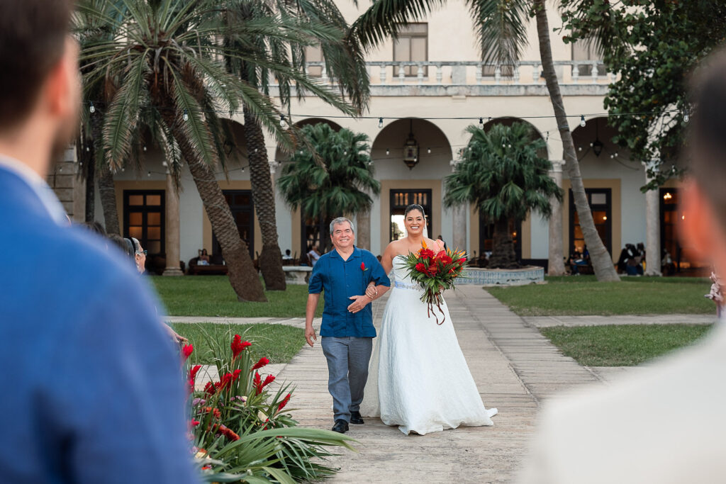 Mara walks arm in arm with her father toward the aisle, with the Hotel Nacional in the background