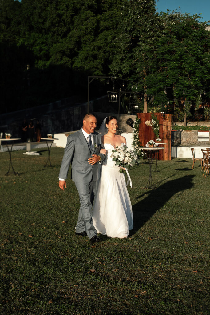 Novia entra del brazo de su padre con ramo de flores blancas en boda en Cuba