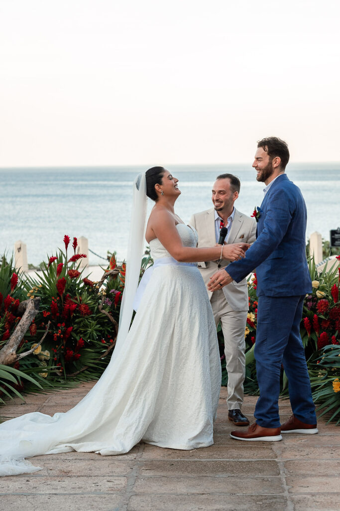 Couple standing during the ceremony with warm-toned flowers and the sea in the background at the Hotel Nacional