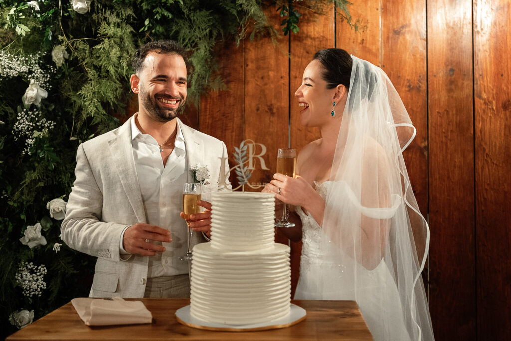 Novios brindan con su pastel nupcial blanco decorado con sus iniciales