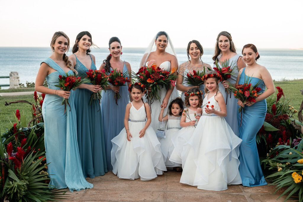 The bride poses with her wedding party and flower girls, with the sea in the background at the Hotel Nacional