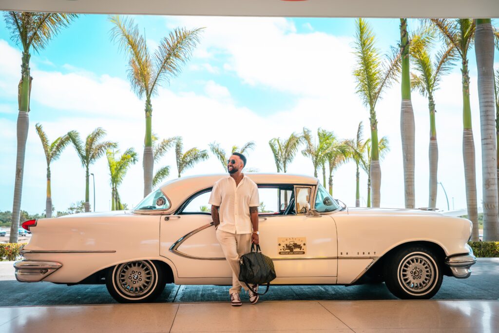 The groom poses with a white classic car in front of the hotel in Varadero