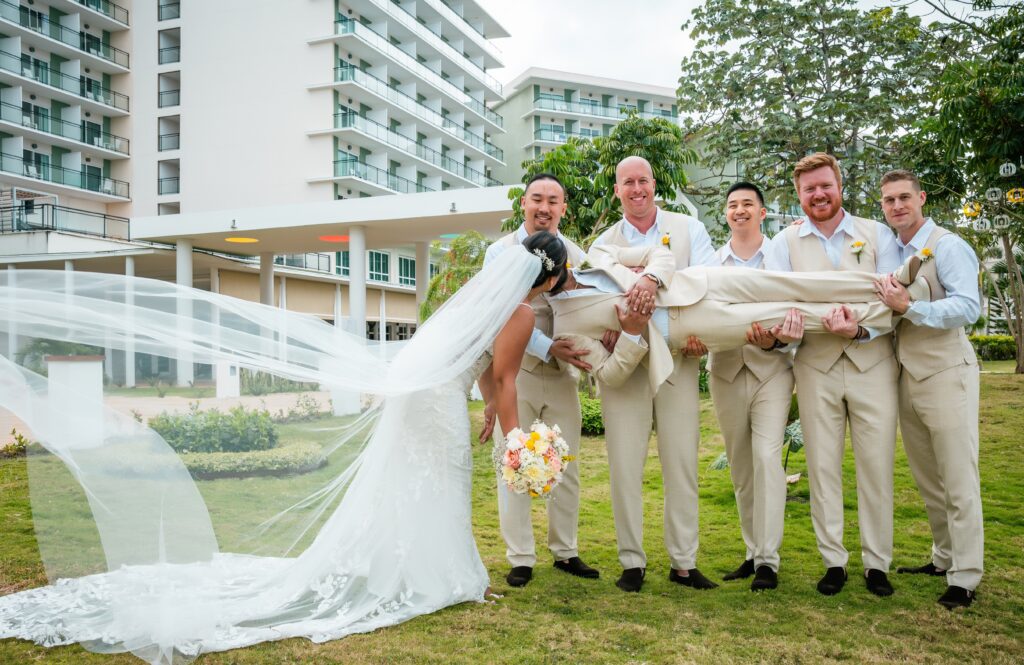 The groomsmen lift the groom while the bride kisses him joyfully