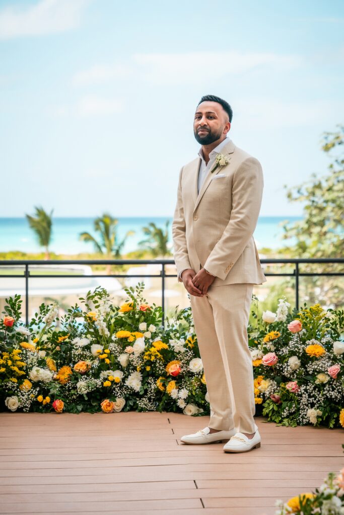 The groom waits standing at the flower-decorated altar by the sea