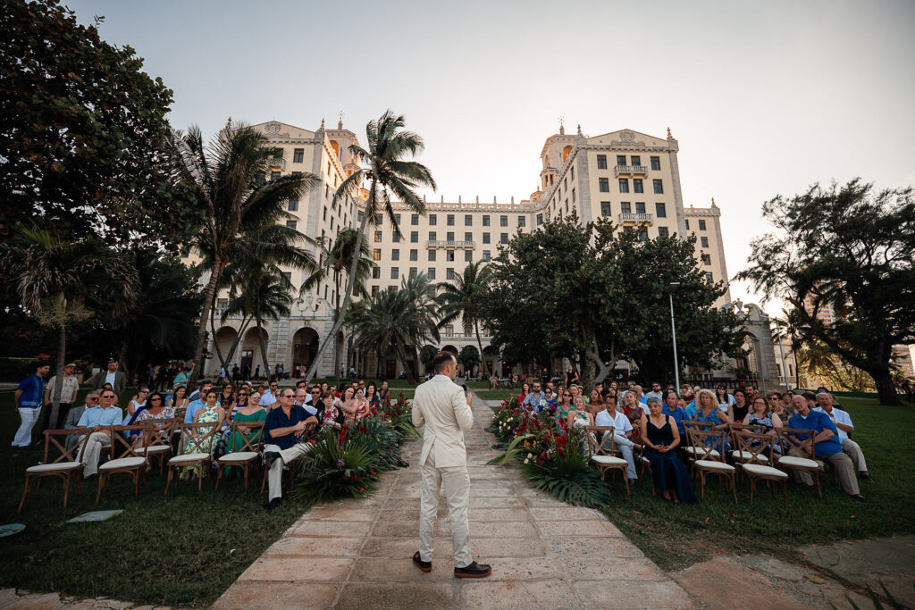 Guests seated with the Hotel Nacional in the background and warm-toned flowers lining the wedding aisle