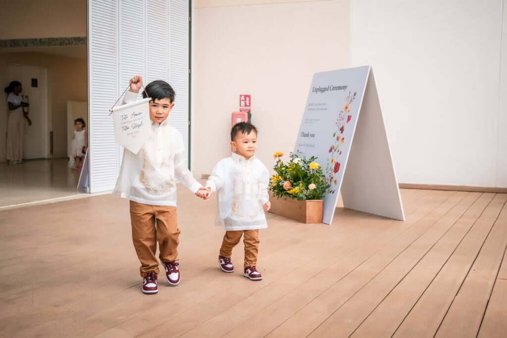 Two ring bearers walk down the aisle with a sign and traditional outfits