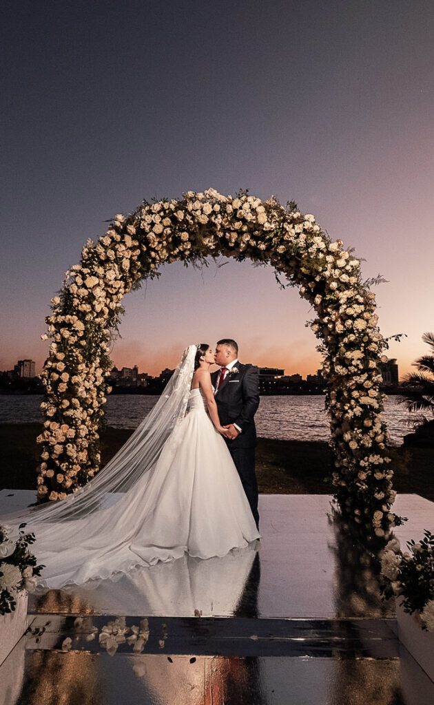 Bride and groom under a floral arch at sunset during their wedding at La Divina Pastora