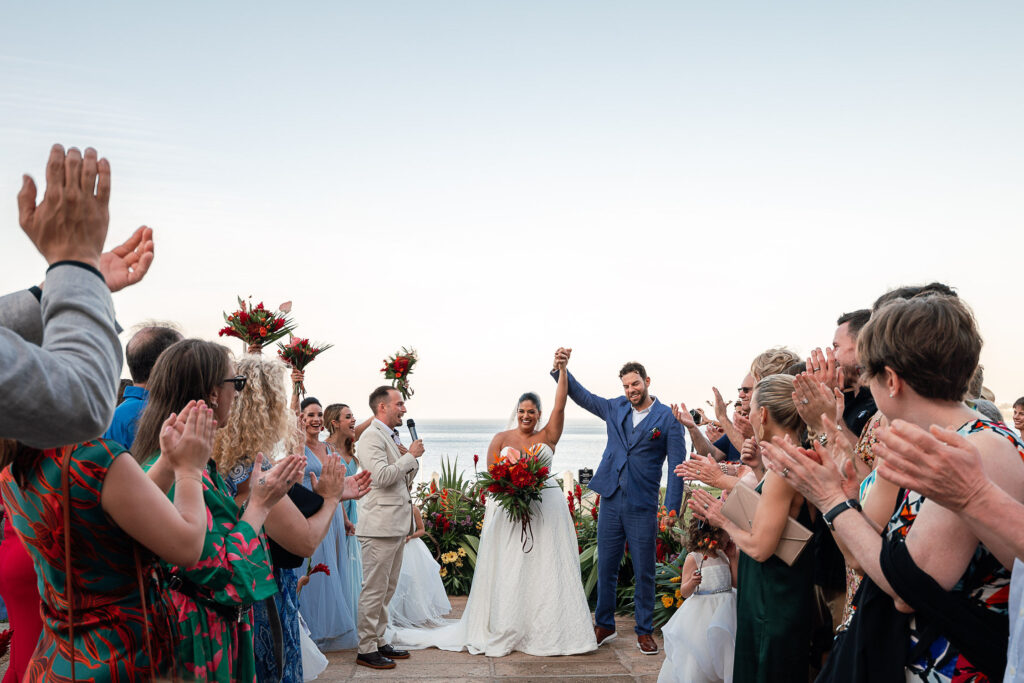 Couple raising their hands as they walk down the aisle surrounded by flowers and guests at the Hotel Nacional